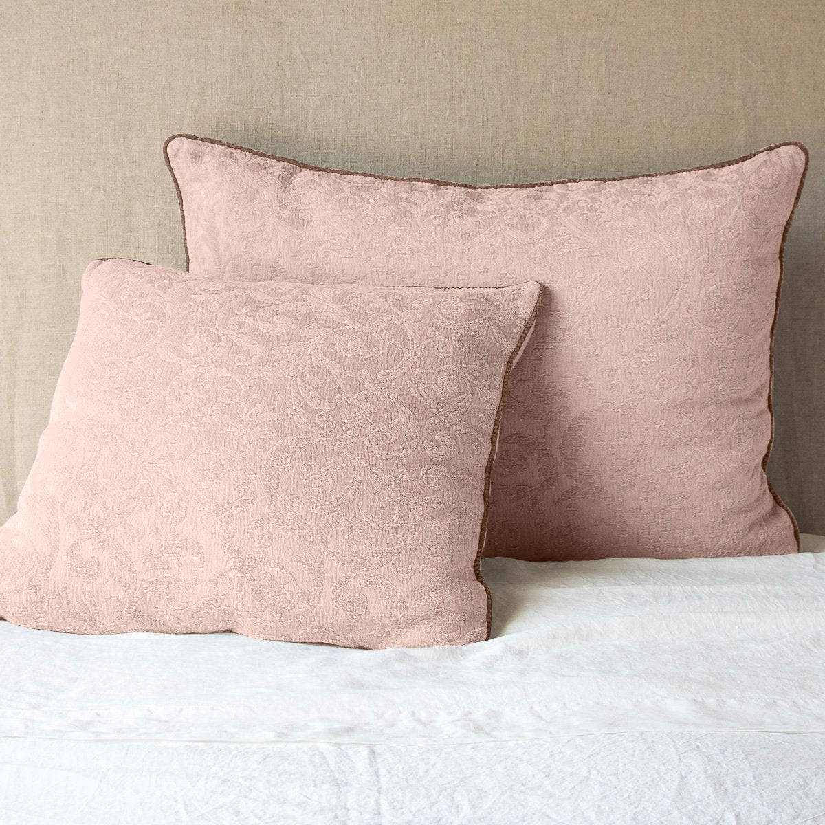 Rouge: Two Adele shams, shown in euro and deluxe sizes, leaning against a neutral toned headboard on white bedding.