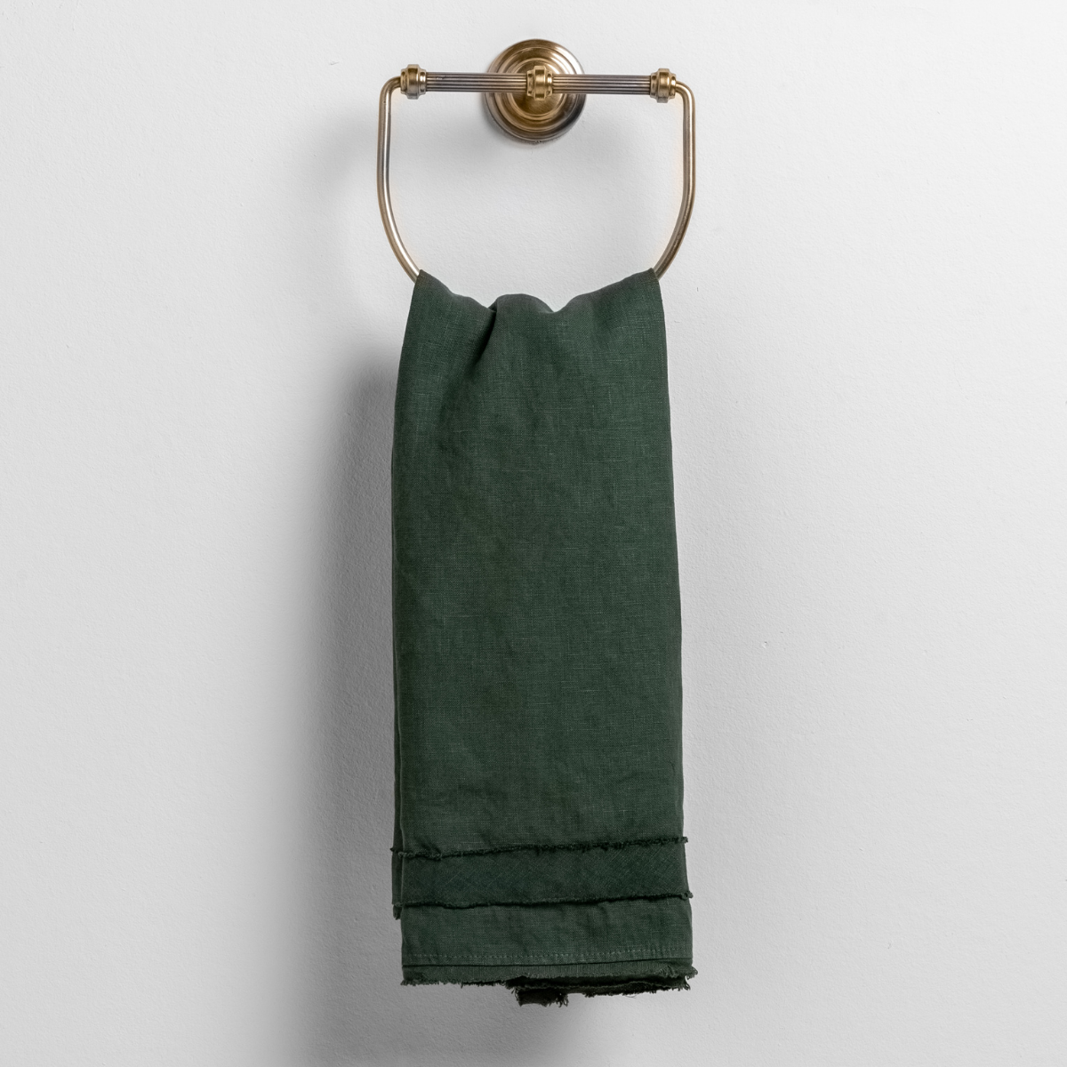 Juniper: midweight linen guest towel with raw edge band at both ends hanging from a towel ring mounted to a white wall. 