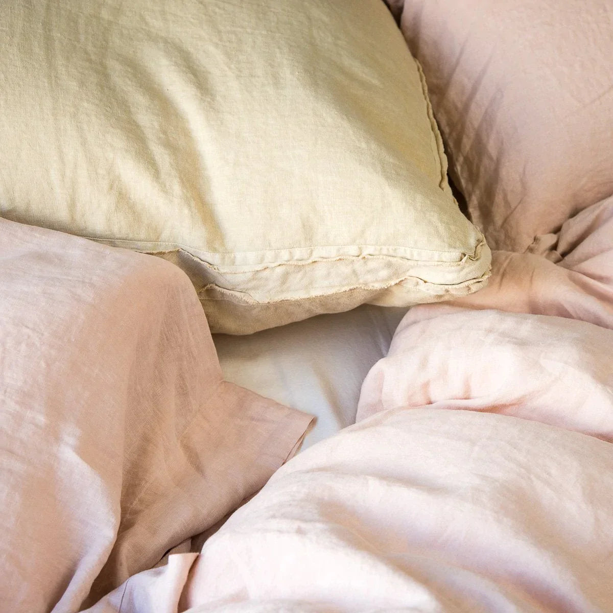 : Austin sham layered with pillows and duvet in pink and gold tones. Close up angle detailing raw edge trim.