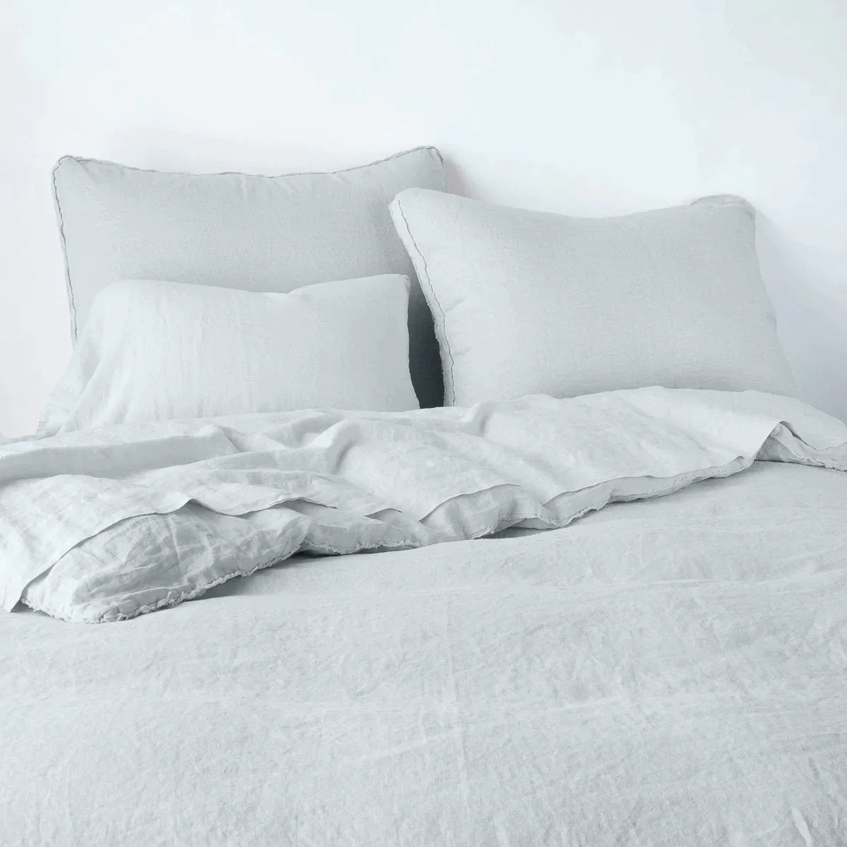 Cloud: Midweight linen shams shown from foot of bed, leaning against a plain background with monochromatic bedding. 