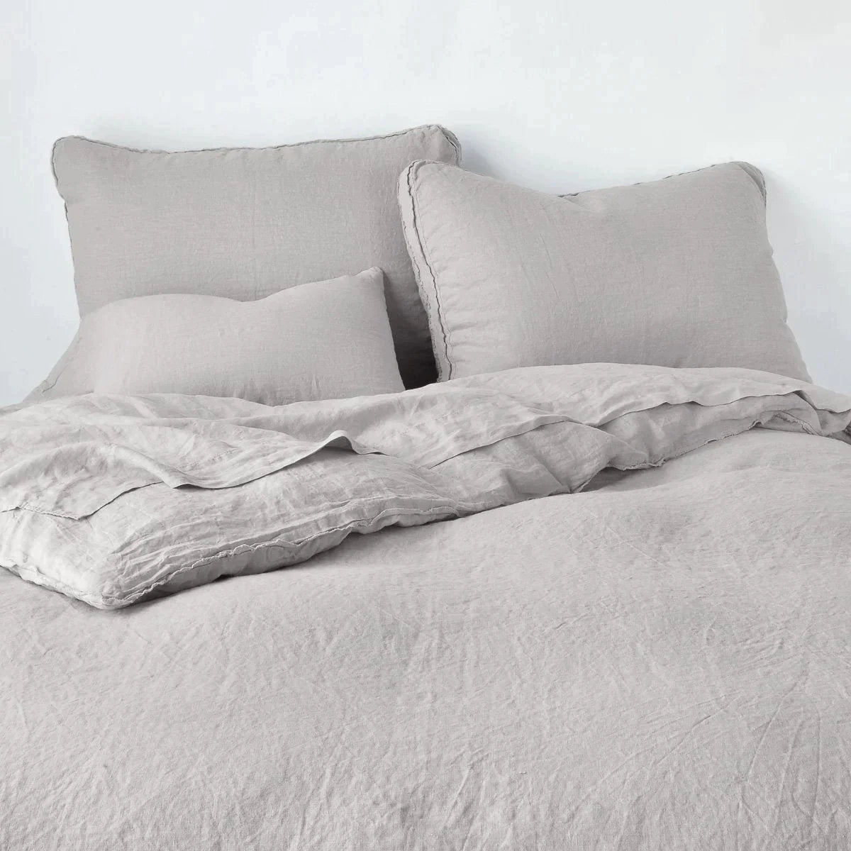 Fog: Midweight linen shams shown from foot of bed, leaning against a plain background with monochromatic bedding. 