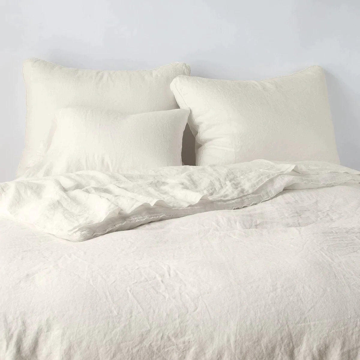 Parchment: Midweight linen shams shown from foot of bed, leaning against a plain background with monochromatic bedding. 