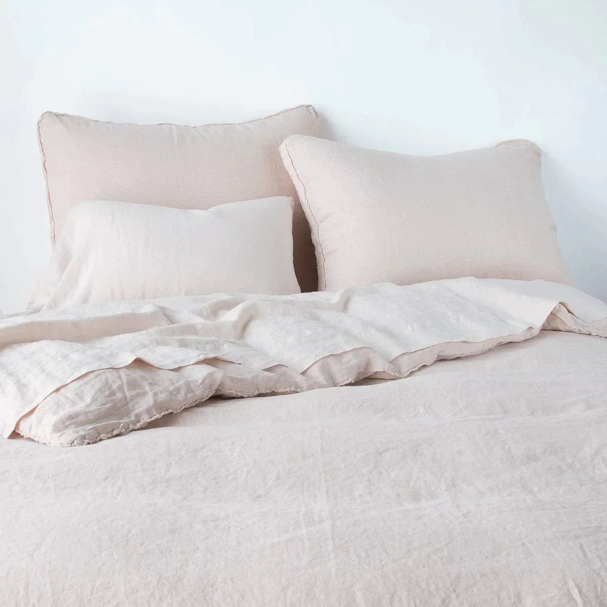 Pearl: Midweight linen shams shown from foot of bed, leaning against a plain background with monochromatic bedding. 