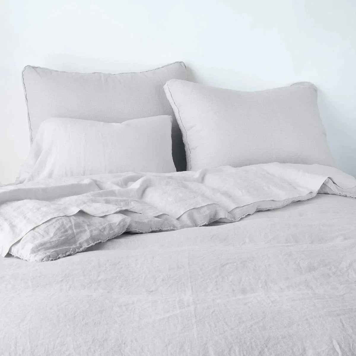 Sterling: Midweight linen shams shown from foot of bed, leaning against a plain background with monochromatic bedding. 