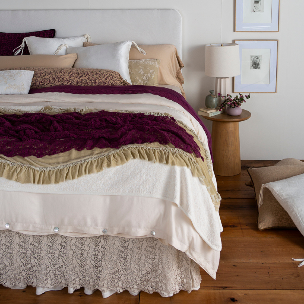 [allvariants]: a 3/4 shot of a bed dressed in neutral tones with pops of color - a lace bolster with a contrasting liner is shown in at the head of the bed. 