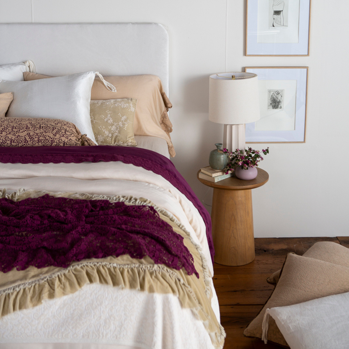 : rumpled lace bed scarf layered ontop of a silk velvet throw blanket at the foot of a bed dressed in light tones with pops of color. 