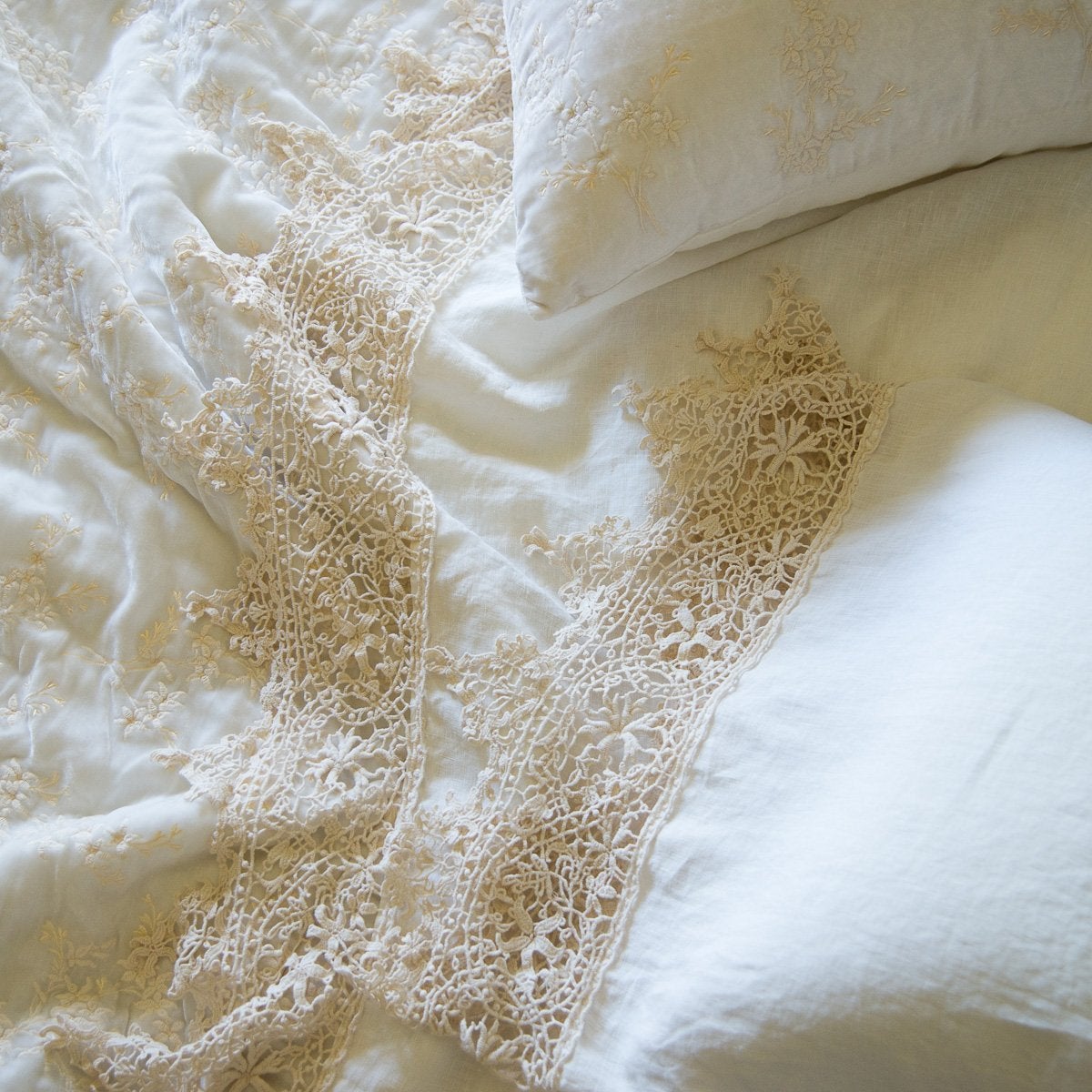 : Close up of a Frida flat sheet and pillowcase, layered over embroidered silk velvet, all in winter white - overhead view.