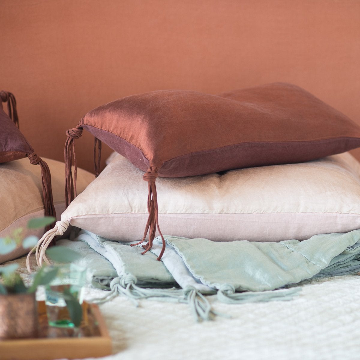 : Taline pillows and folded blanket stacked, showcasing hand-tied tassels - side view.