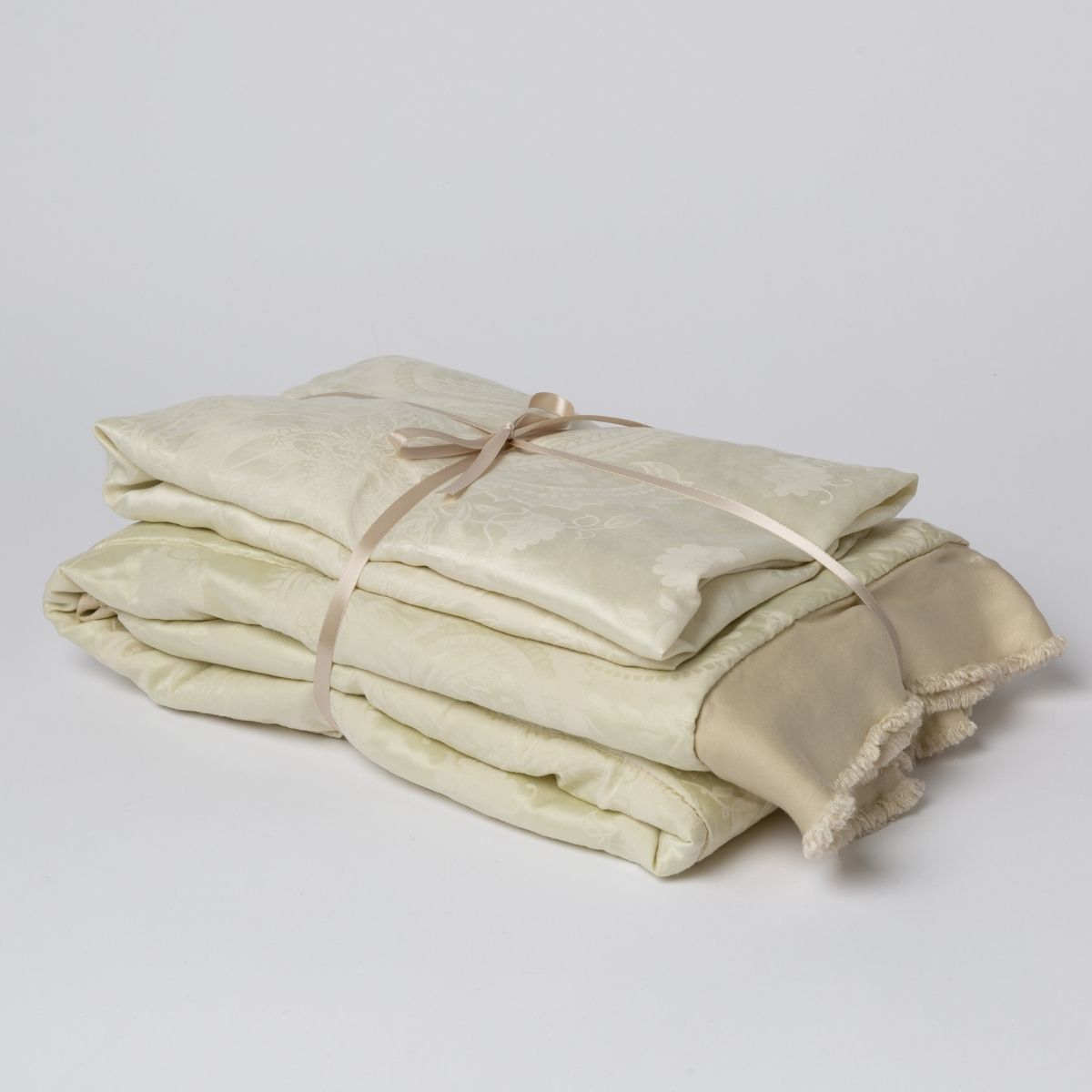 Parchment:  matching crib sheet and baby blanket bundled and tied with a ribbon against a white background.