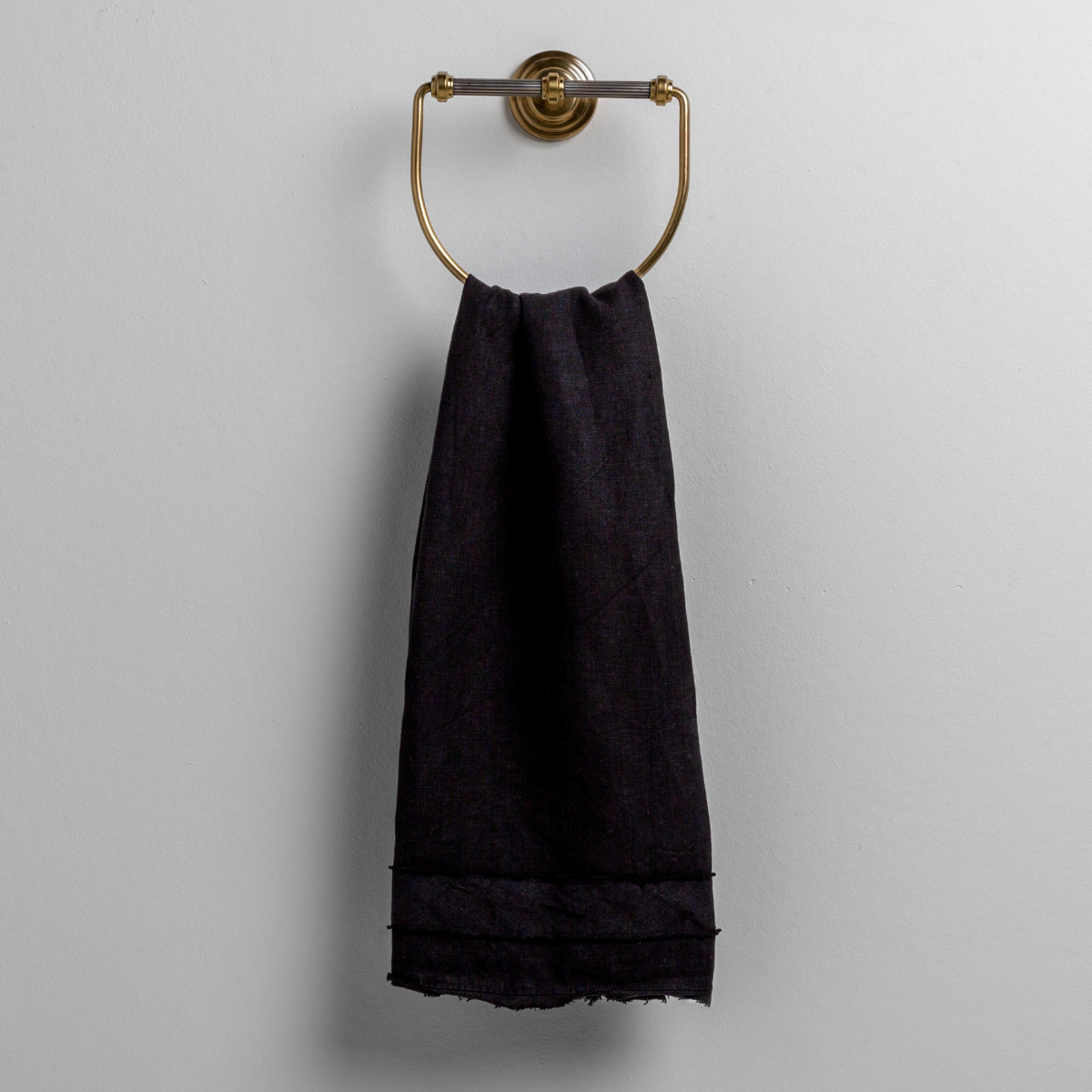 Corvino: midweight linen guest towel with raw edge band at both ends hanging from a towel ring mounted to a white wall. 
