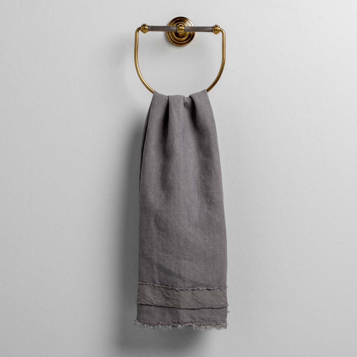 Moonlight: midweight linen guest towel with raw edge band at both ends hanging from a towel ring mounted to a white wall. 