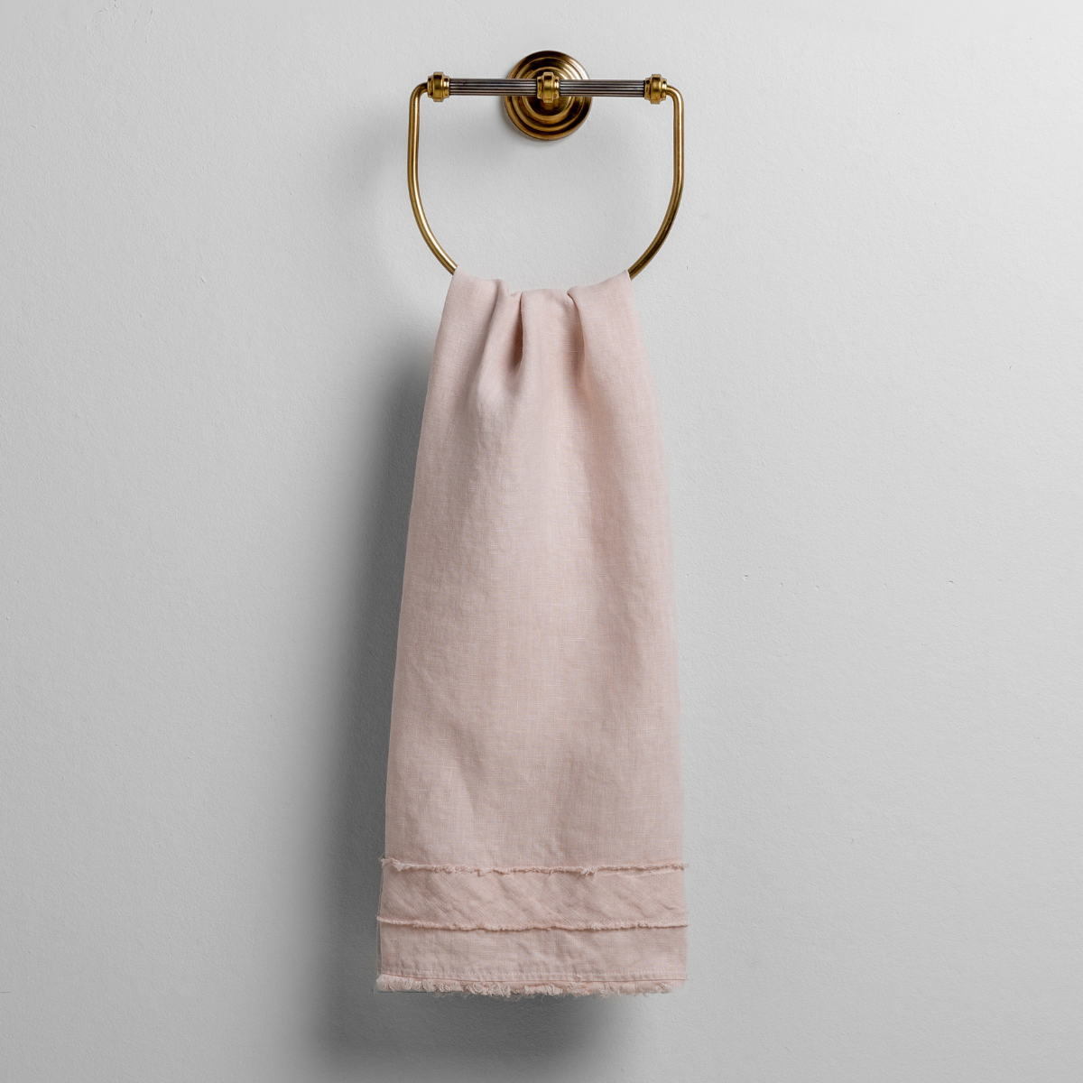 Pearl: midweight linen guest towel with raw edge band at both ends hanging from a towel ring mounted to a white wall. 