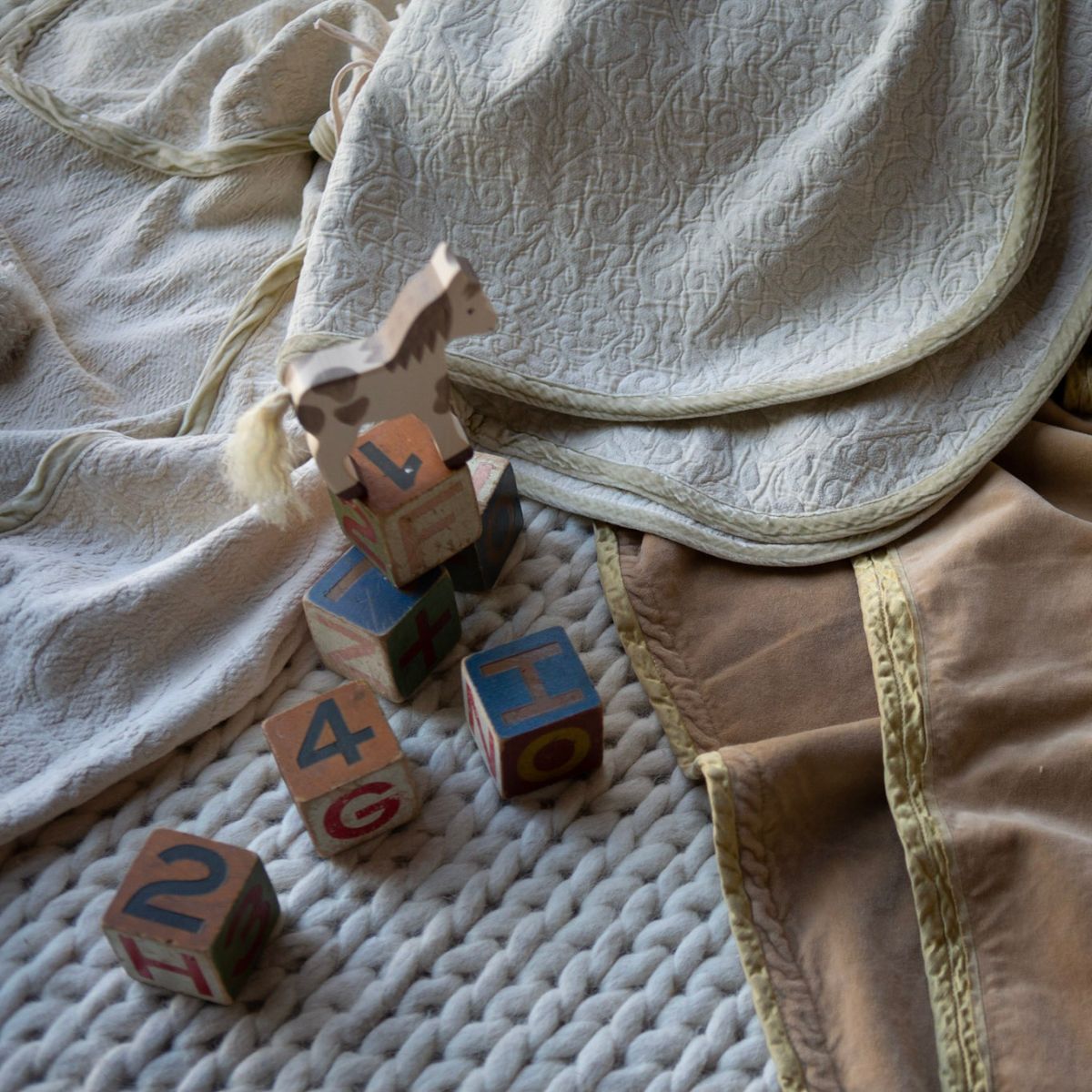 [allvariants]: three baby blankets strewn on the floor with wooden toys scattered on a braided rug.