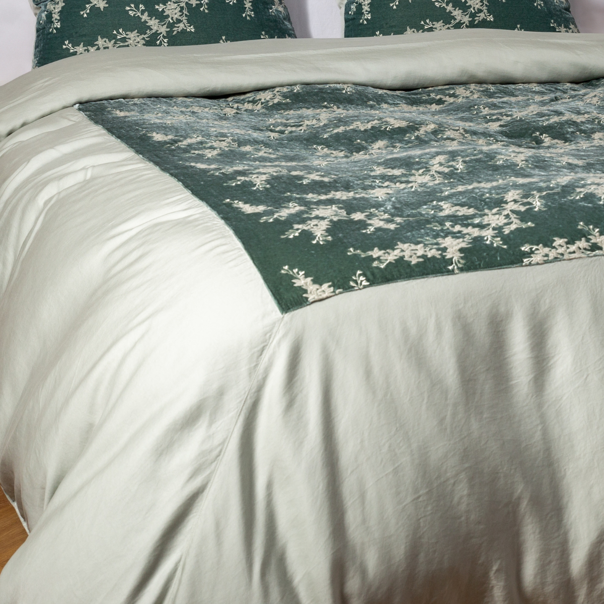 Eucalyptus: A close-up of the mitered corner of an embroidered silk velvet and tencel duvet cover — its matching shams barely visible in the shot. 