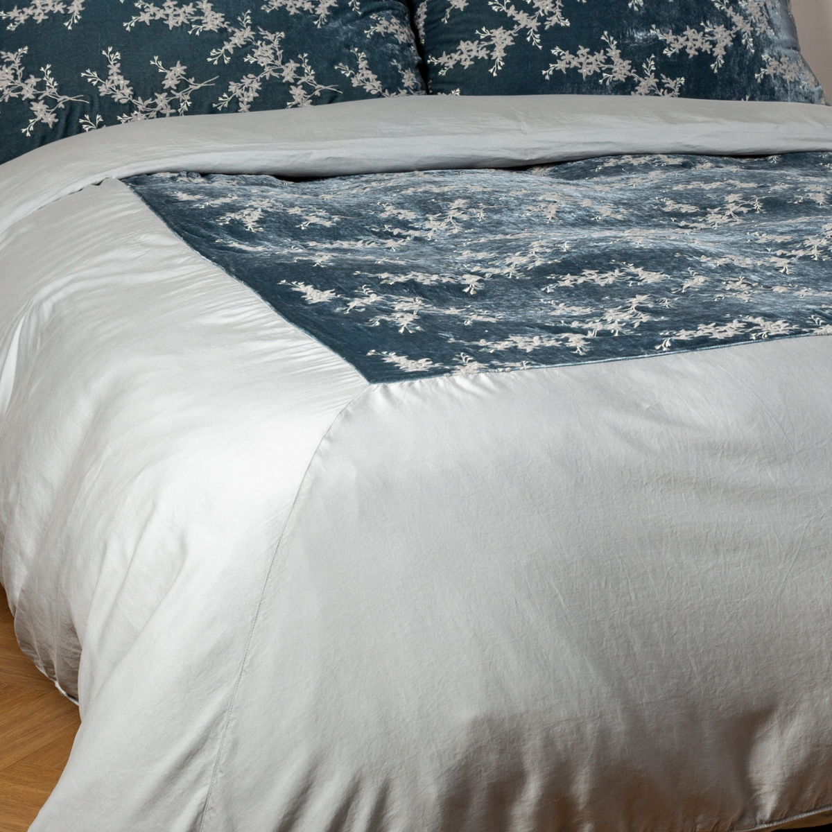 Mineral: A close-up of the mitered corner of an embroidered silk velvet and tencel duvet cover — its matching shams barely visible in the shot. 