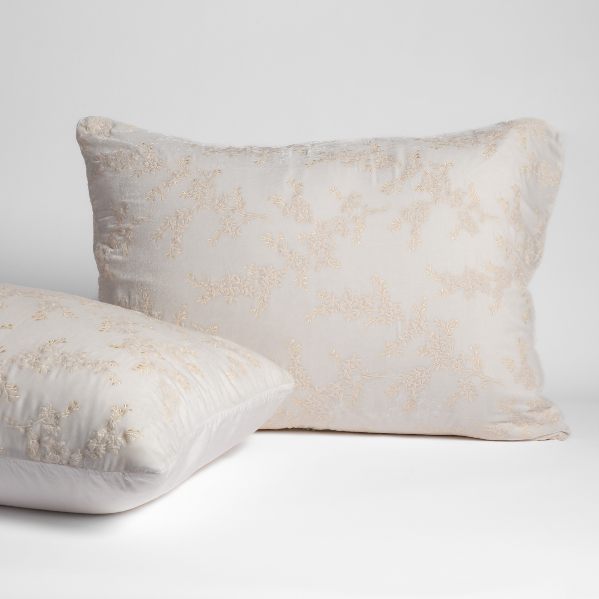 Winter White: A pair of shams shown against a white background with one sham upright and the other on its side to show the tencel back and embroidered silk velvet face. 