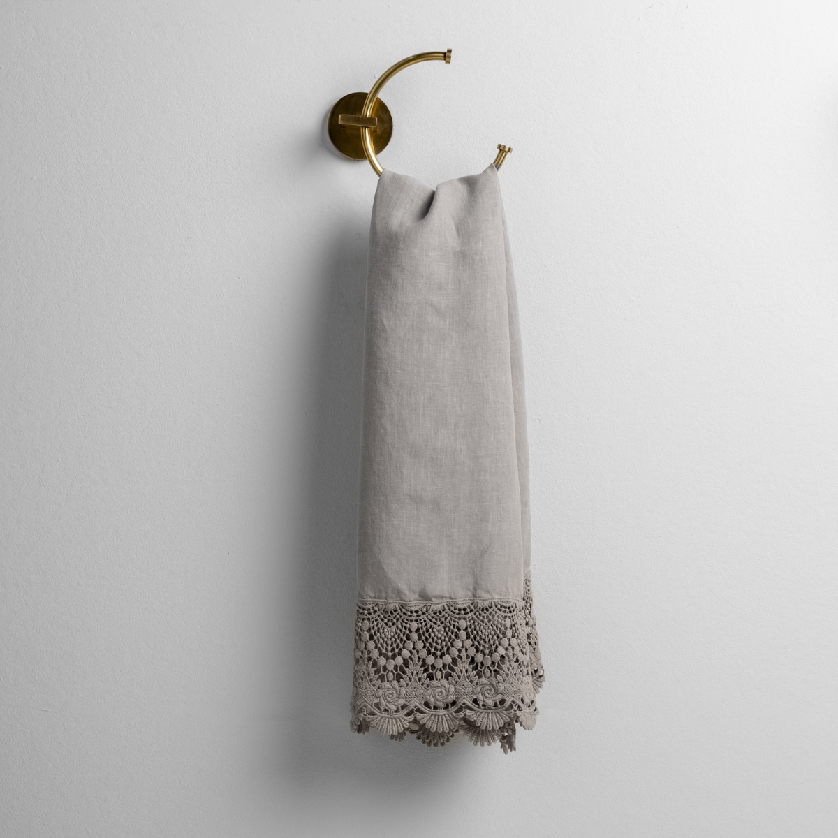 Mineral linen with mattine lace trimmed guest towel on a decorative towel ring mounted on a white wall. 