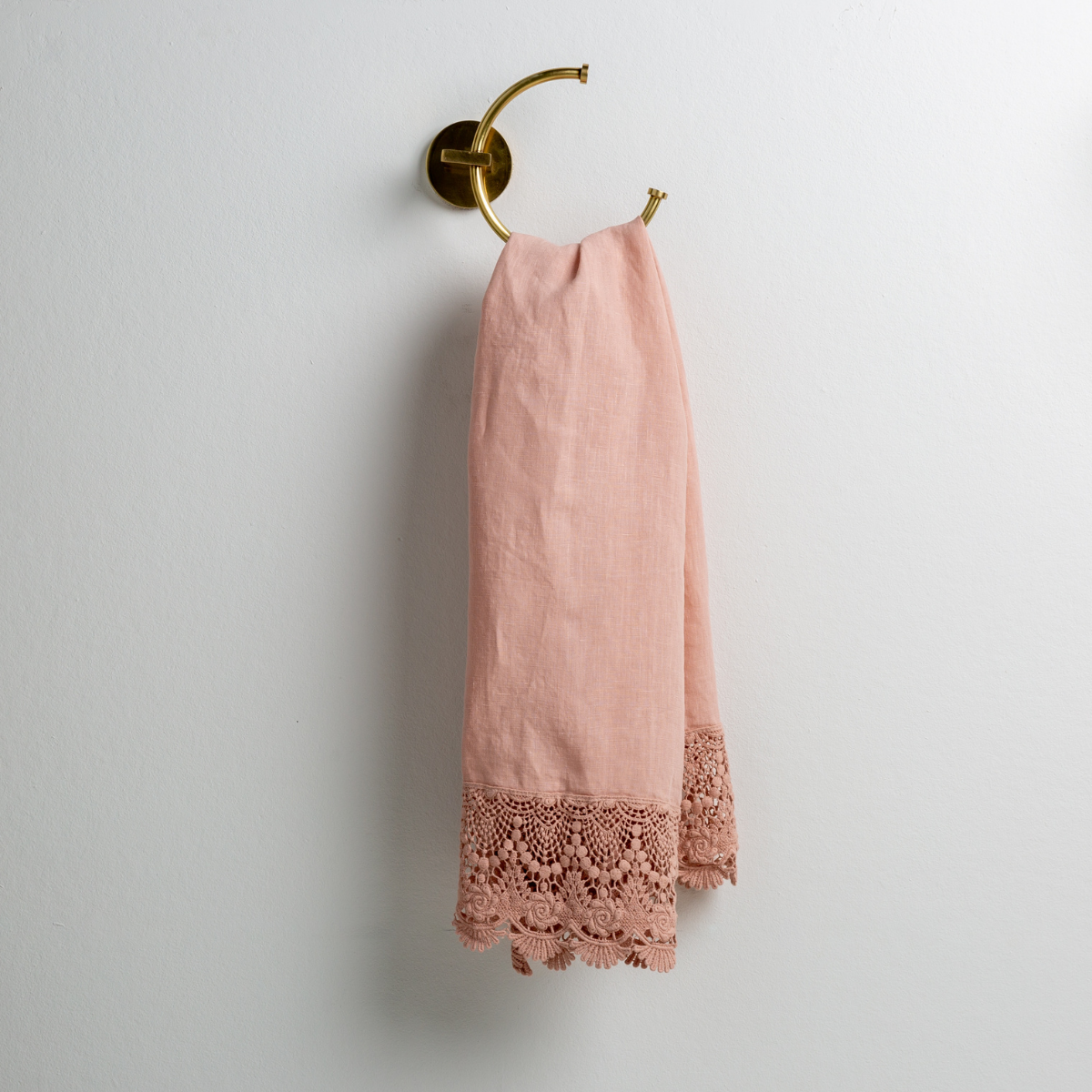 Rouge: linen with mattine lace trimmed guest towel on a decorative towel ring mounted on a white wall. 