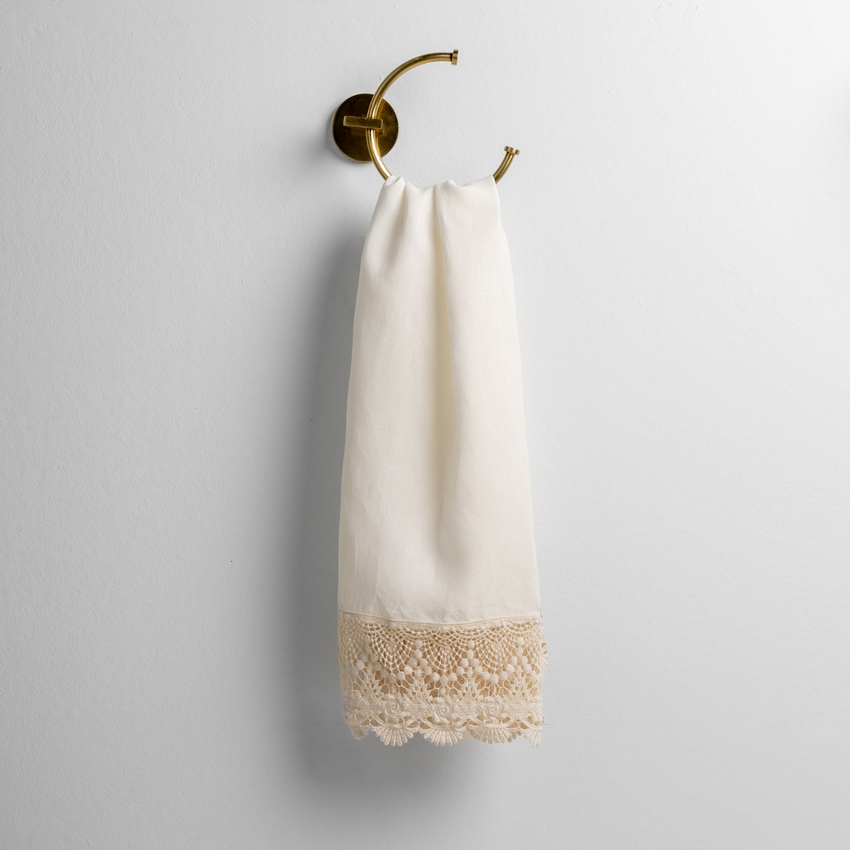 Winter White: linen with mattine lace trimmed guest towel on a decorative towel ring mounted on a white wall. 