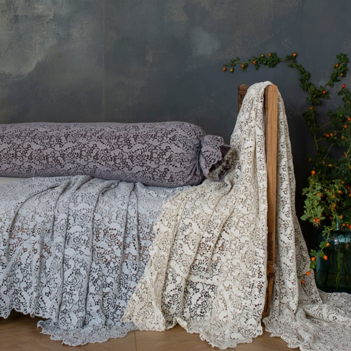 : lace bolster cover on a bench with lace bed scarves against a limewash background. 