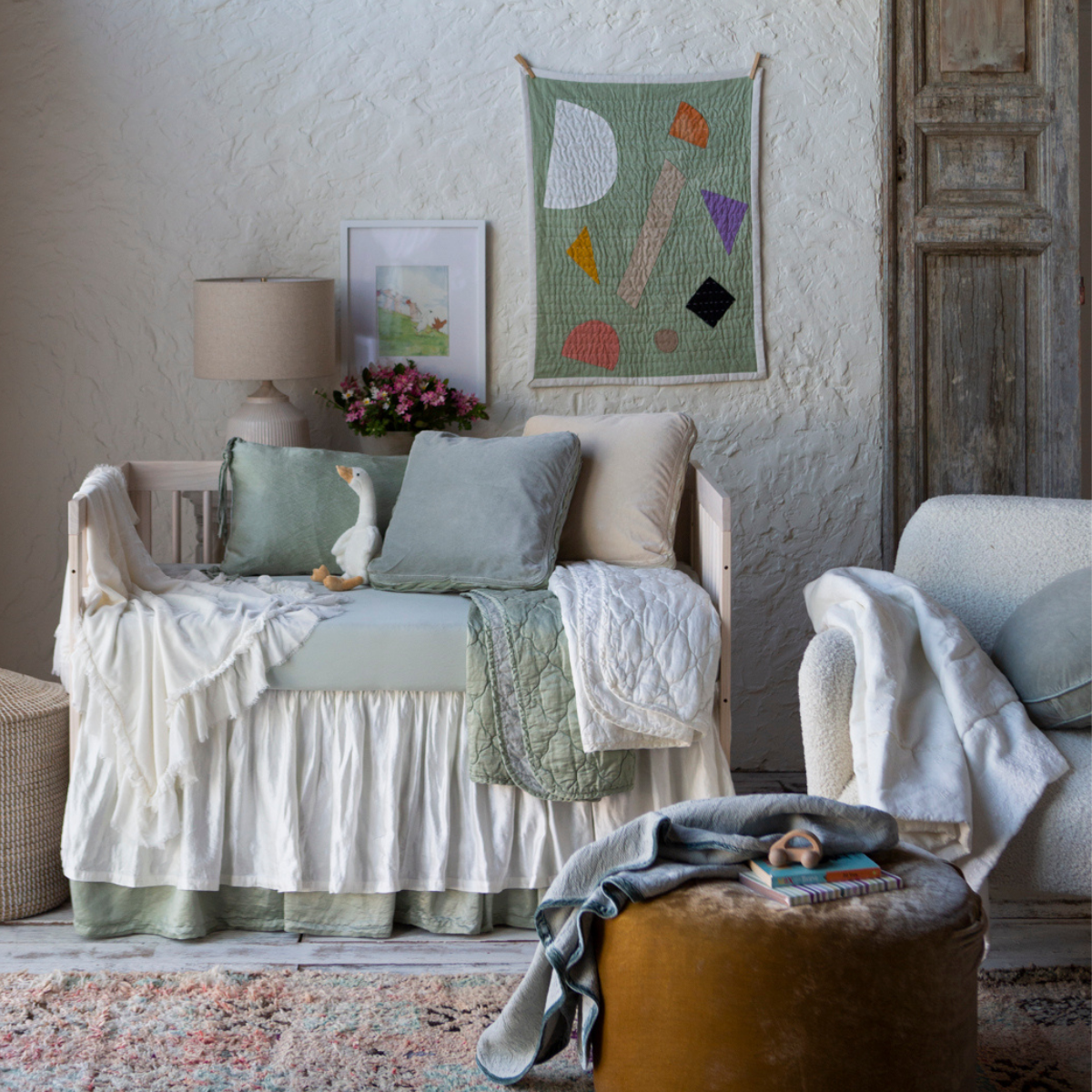 [allvariants]: Winter white crib skirt shown layered over a soft green crib skirt in a nursery scene with the same tones and various textures.