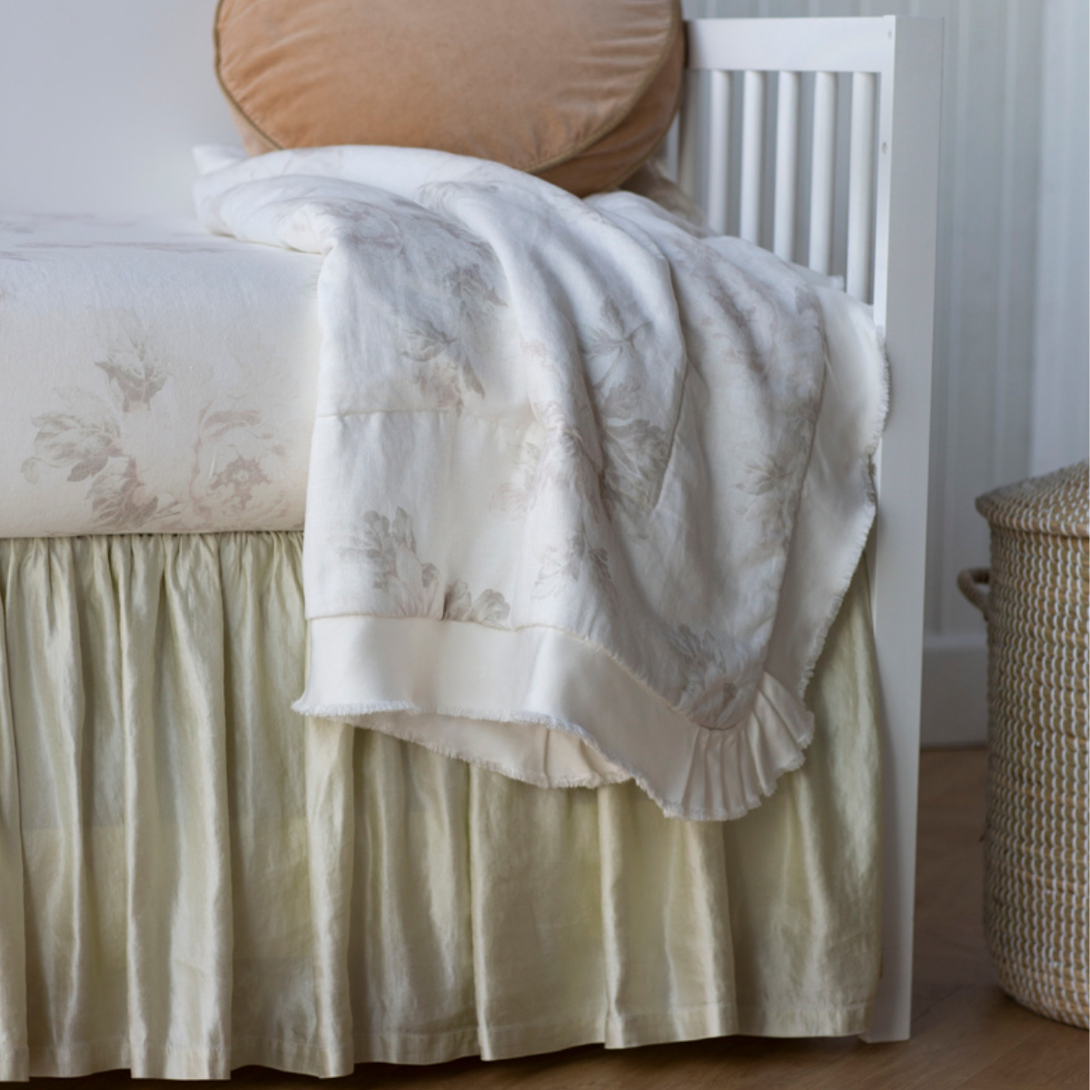 : Close up of blanket draped over crib sheet and charmeuse crib skirt, highlighting the soft floral pattern.