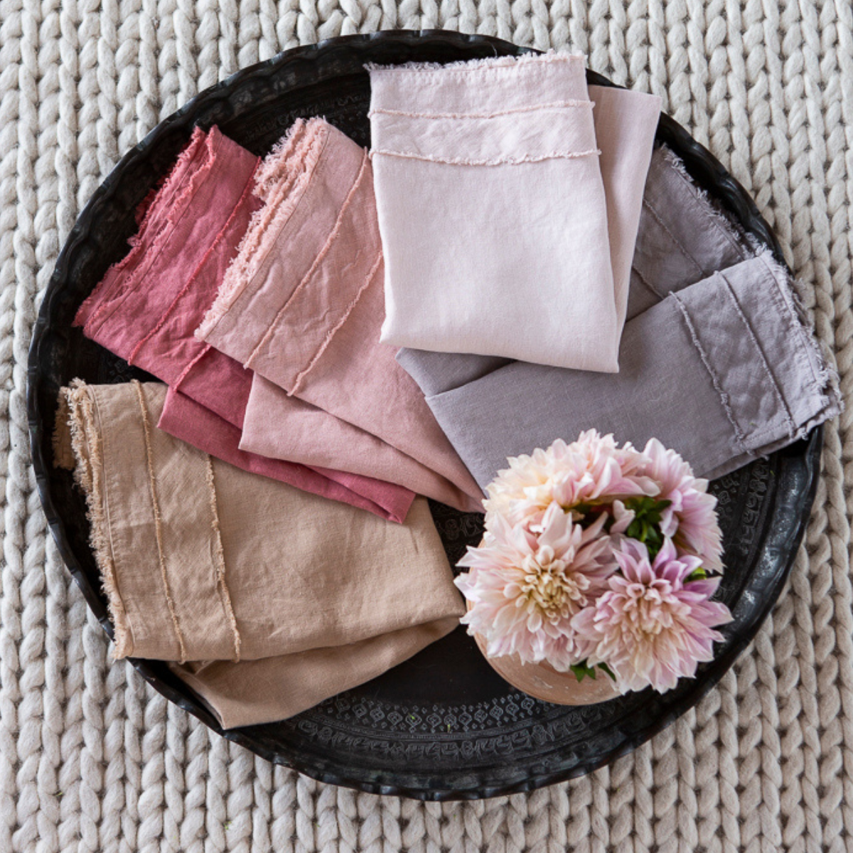 : an overhead shot of folded midweight linen guest towels with banded edges with raw edges - shown with fresh flowers.