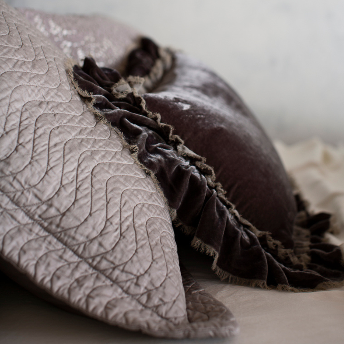 [allvariants]: close up of the side view of a quilted cotton sateen sham with silk velvet throw pillow with raw edges propped up against the pillow sham - both in grey tones. 
