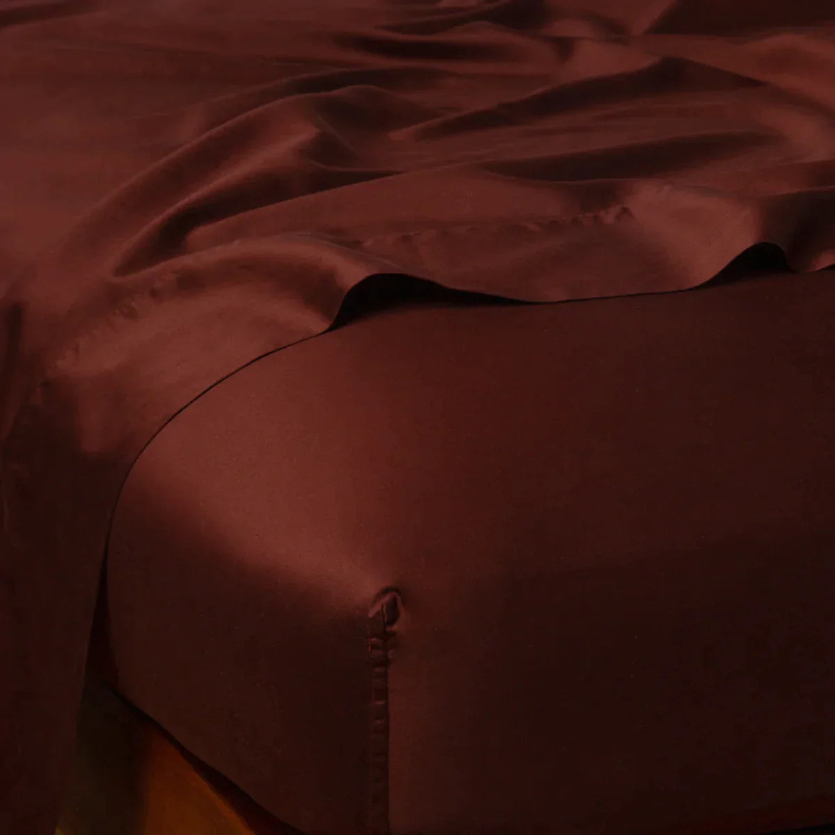 Mahogany: Cotton sateen flat sheet draped over matching fitted sheet. Shown from the top corner, the flat sheet is rumpled, highlighting the shine of the fabric.