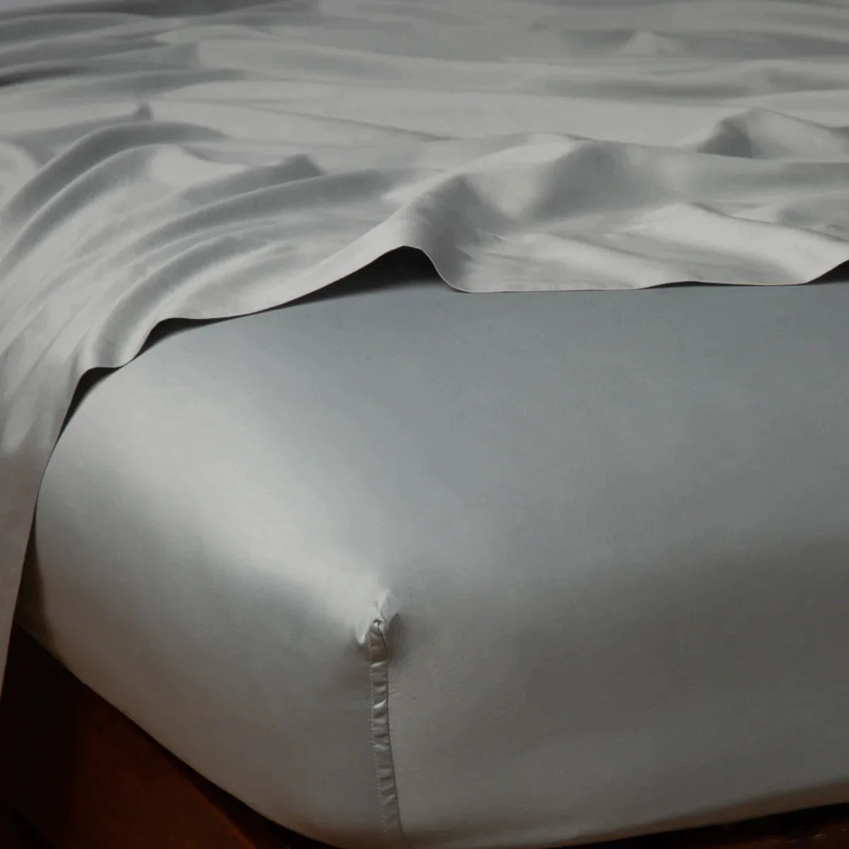 Mineral: Cotton sateen flat sheet draped over matching fitted sheet. Shown from the top corner, the flat sheet is rumpled, highlighting the shine of the fabric.