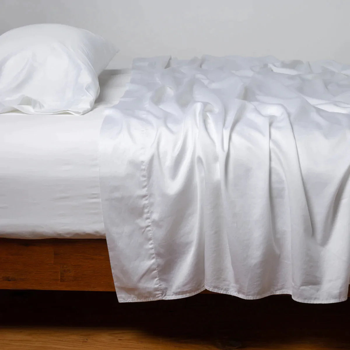 White: Cotton sateen sleeping pillow, on a bed with matching sheets - side view.