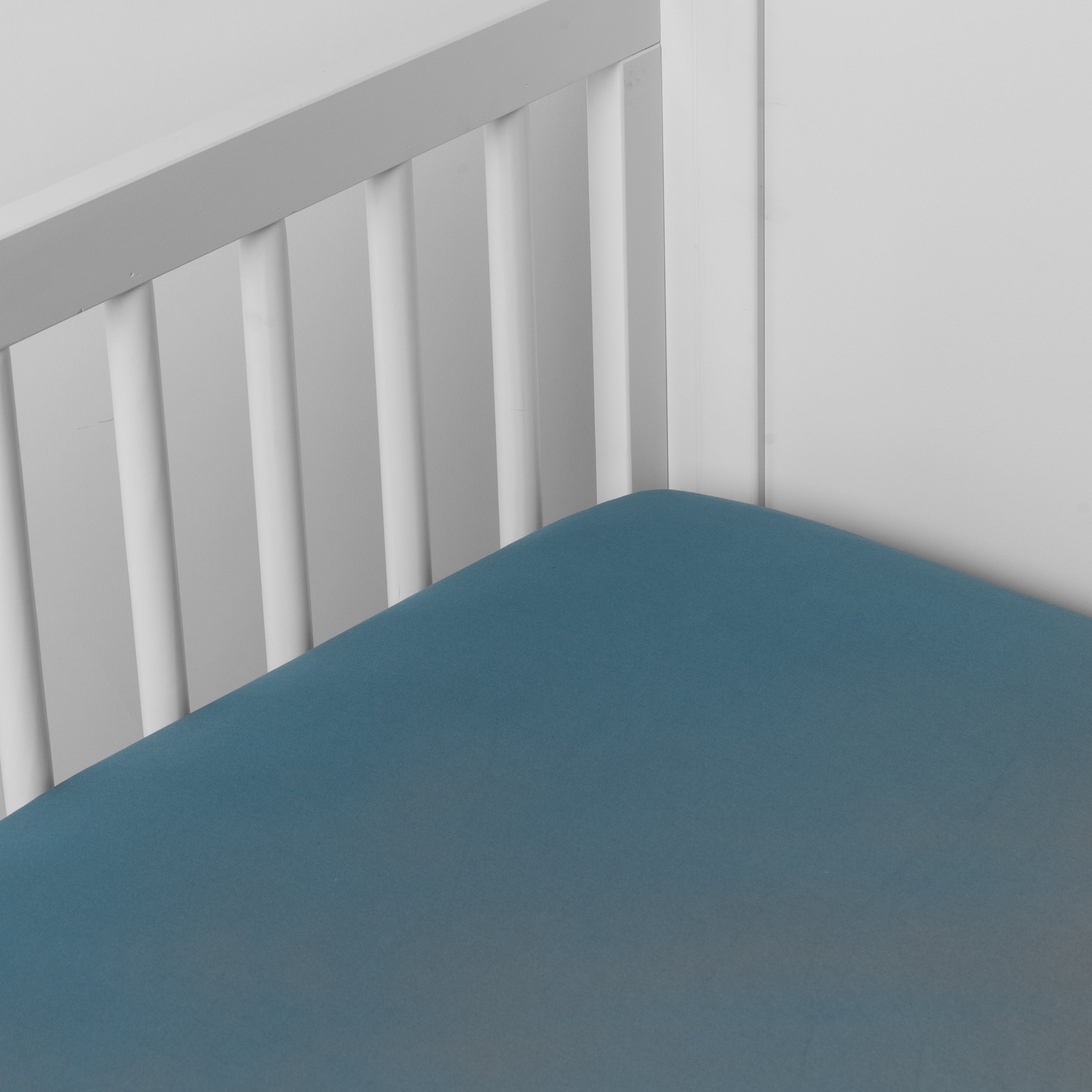 Cenote: Cotton sateen crib sheet shown from a slight overhead angle into  an inside corner of a crib. 