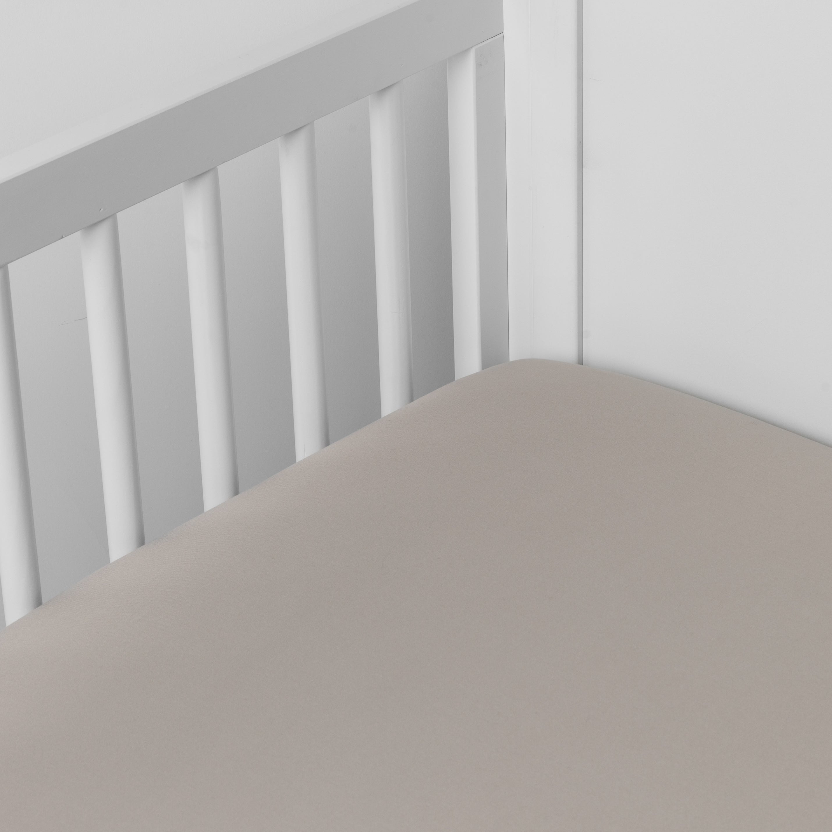 Fog: Cotton sateen crib sheet shown from a slight overhead angle into  an inside corner of a crib. 