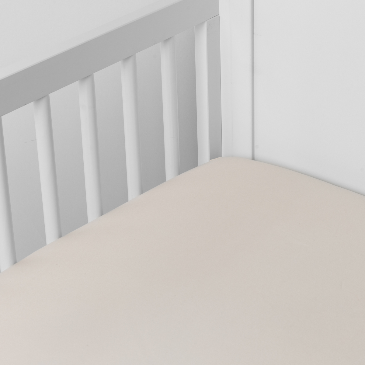 Parchment: Cotton sateen crib sheet shown from a slight overhead angle into  an inside corner of a crib. 