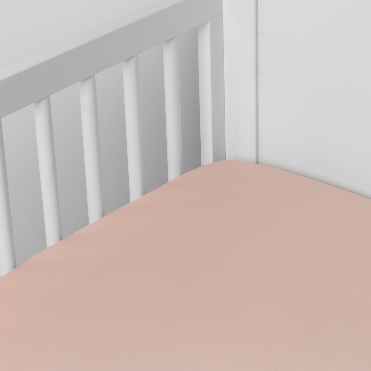 Rouge: Cotton sateen crib sheet shown from a slight overhead angle into  an inside corner of a crib. 