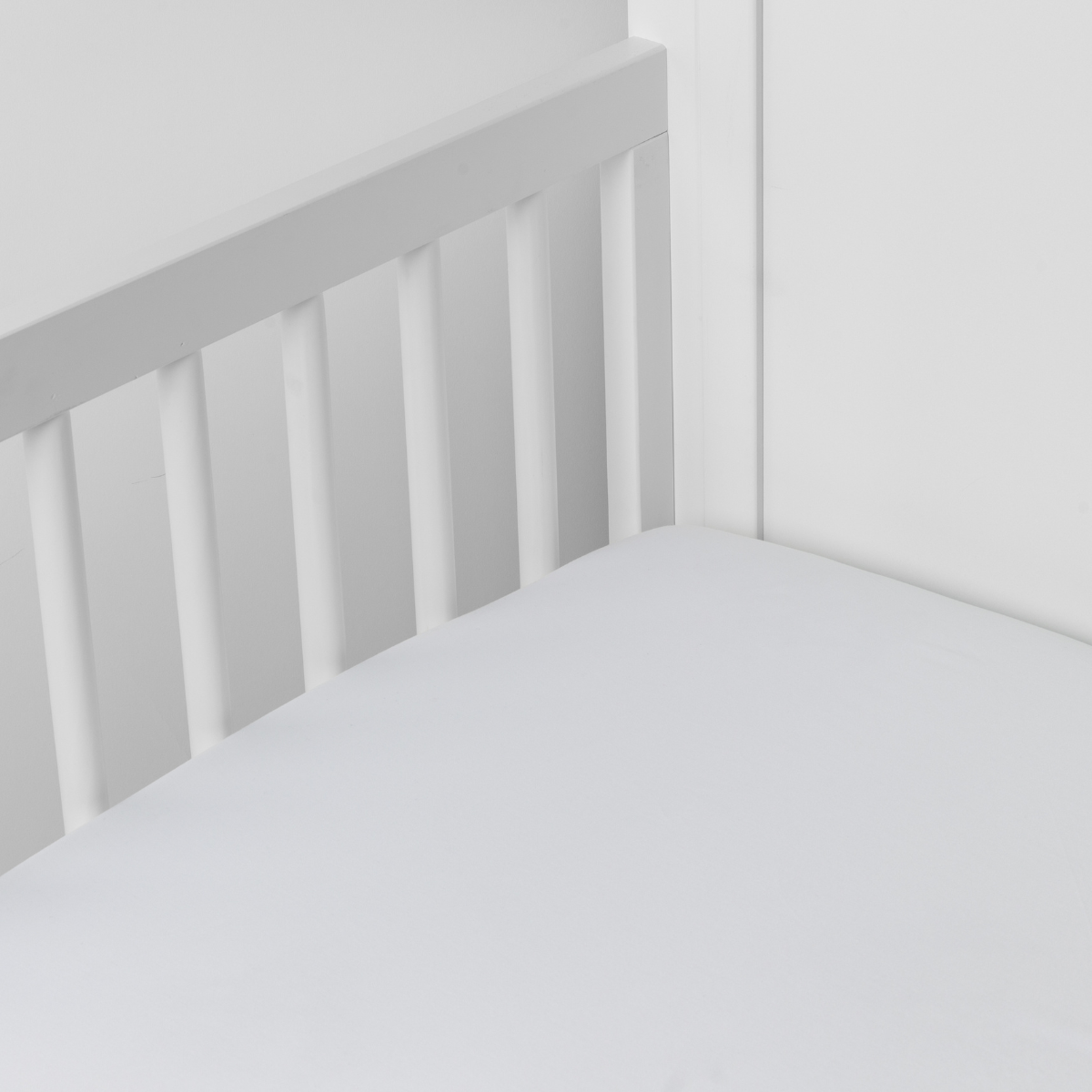 White: Cotton sateen crib sheet shown from a slight overhead angle into  an inside corner of a crib. 