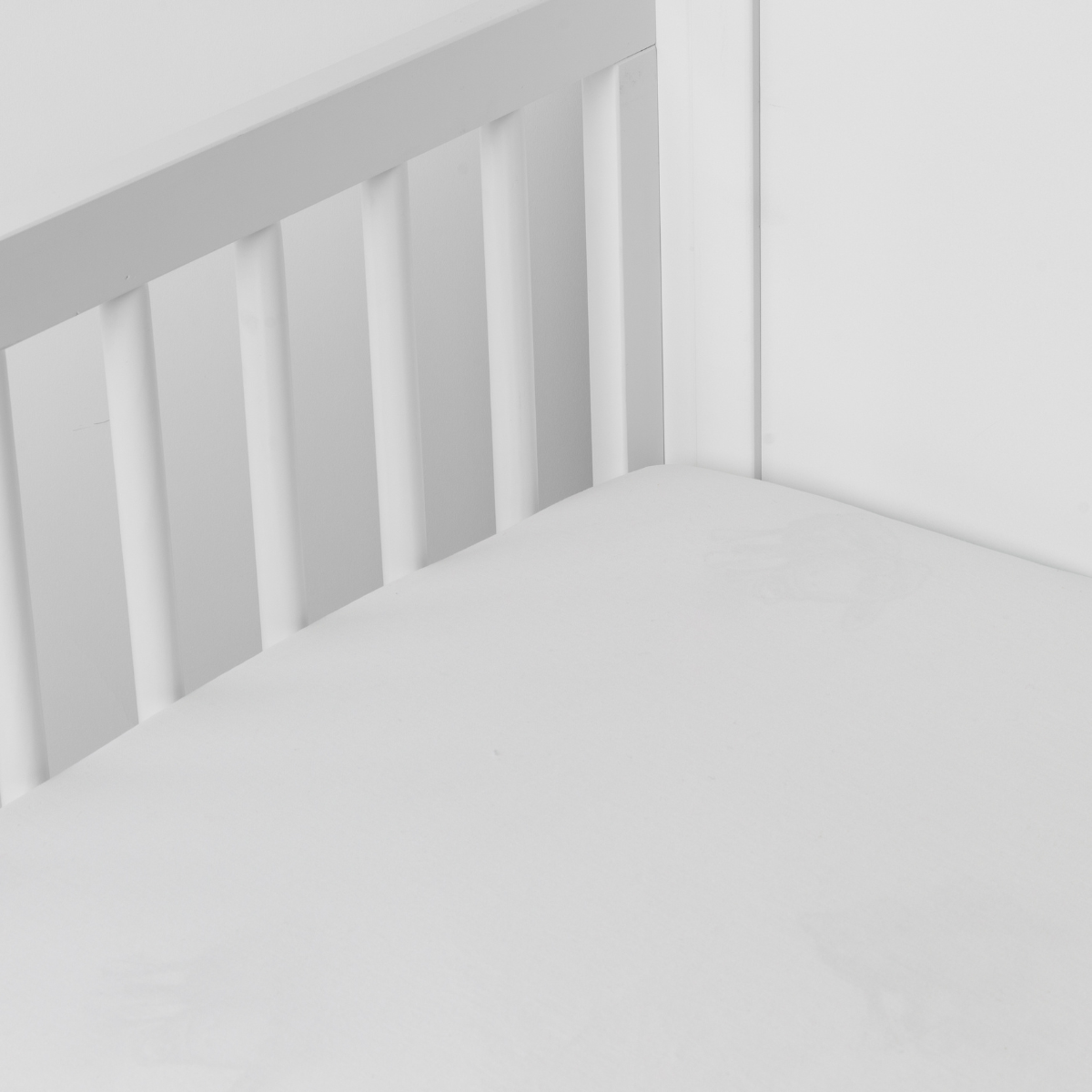 Winter White: Cotton sateen crib sheet shown from a slight overhead angle into  an inside corner of a crib. 