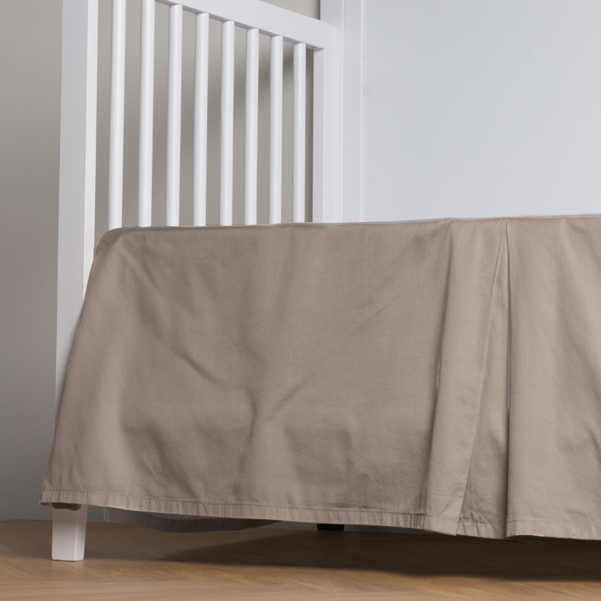 Fog:  cotton sateen cribi skirt with a center pleat shown straight on from a slight angle in a crib without a crib mattress. 