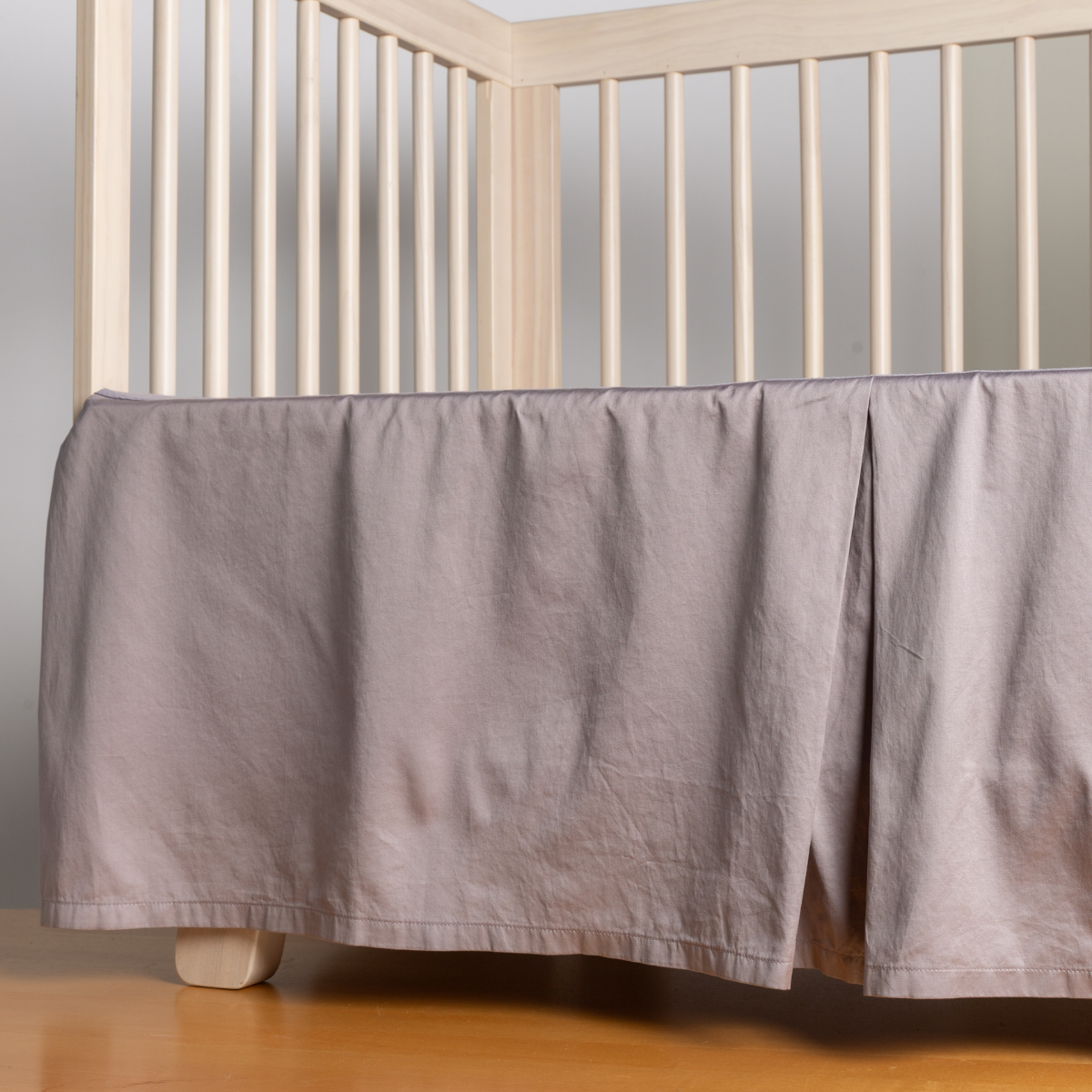 French Lavender: cotton sateen crib skir tiwth a center pleat shown straight on from a slight angle in a crib without a crib mattress. 