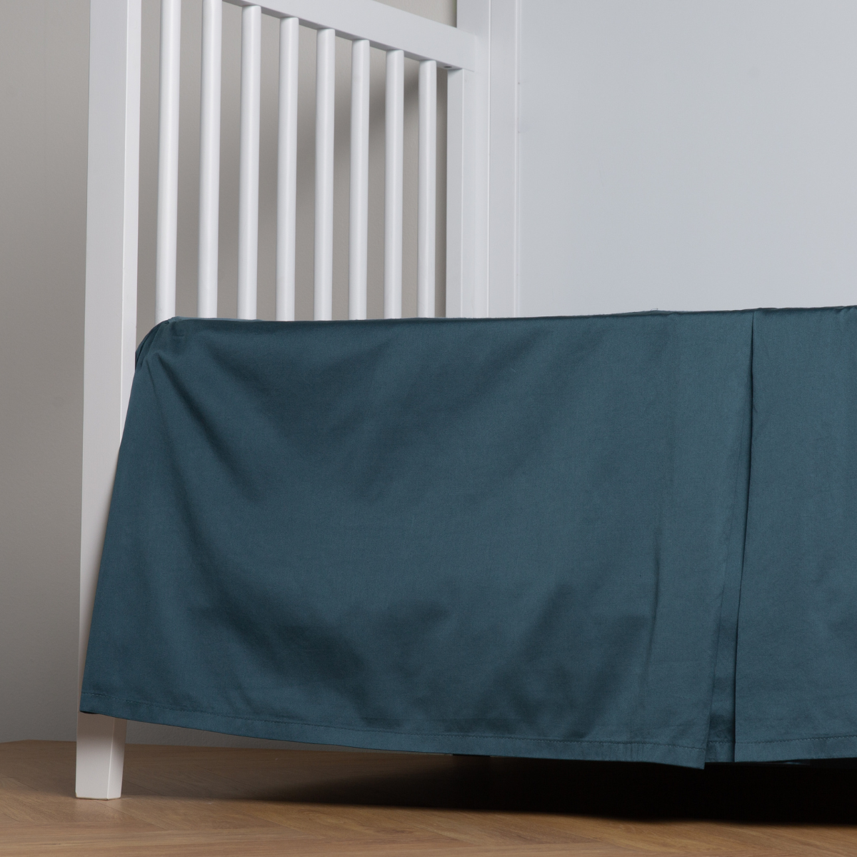 Midnight:  cotton sateen cribi skirt with a center pleat shown straight on from a slight angle in a crib without a crib mattress. 