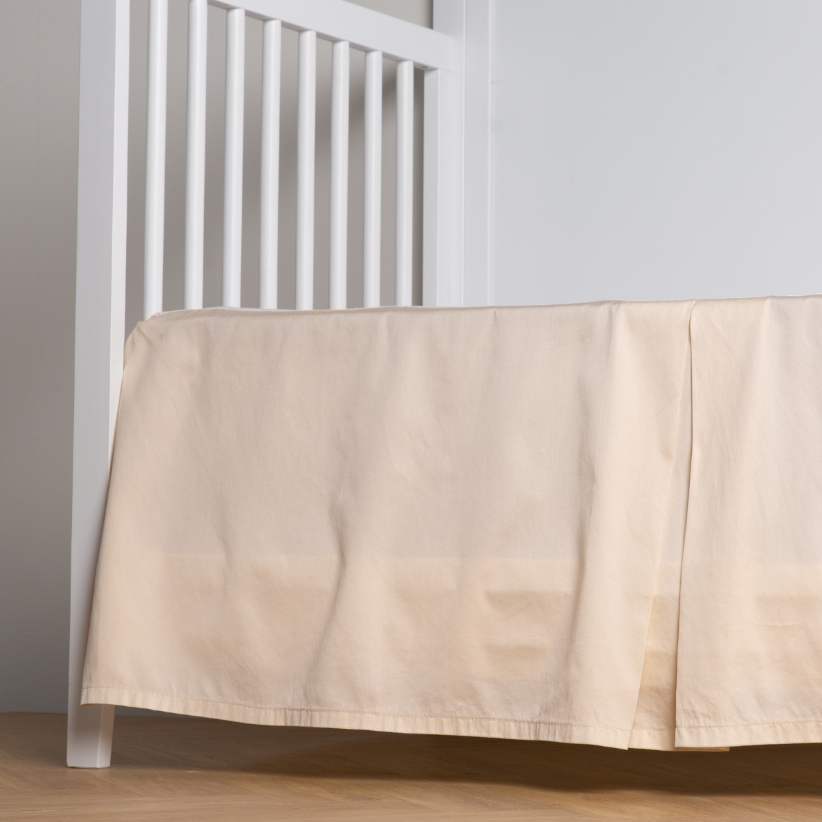 Parchment: cotton sateen cribi skirt with a center pleat shown straight on from a slight angle in a crib without a crib mattress. 