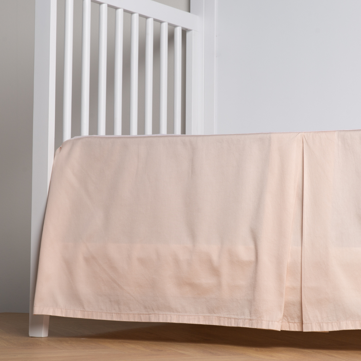 Pearl: cotton sateen cribi skirt with a center pleat shown straight on from a slight angle in a crib without a crib mattress. 