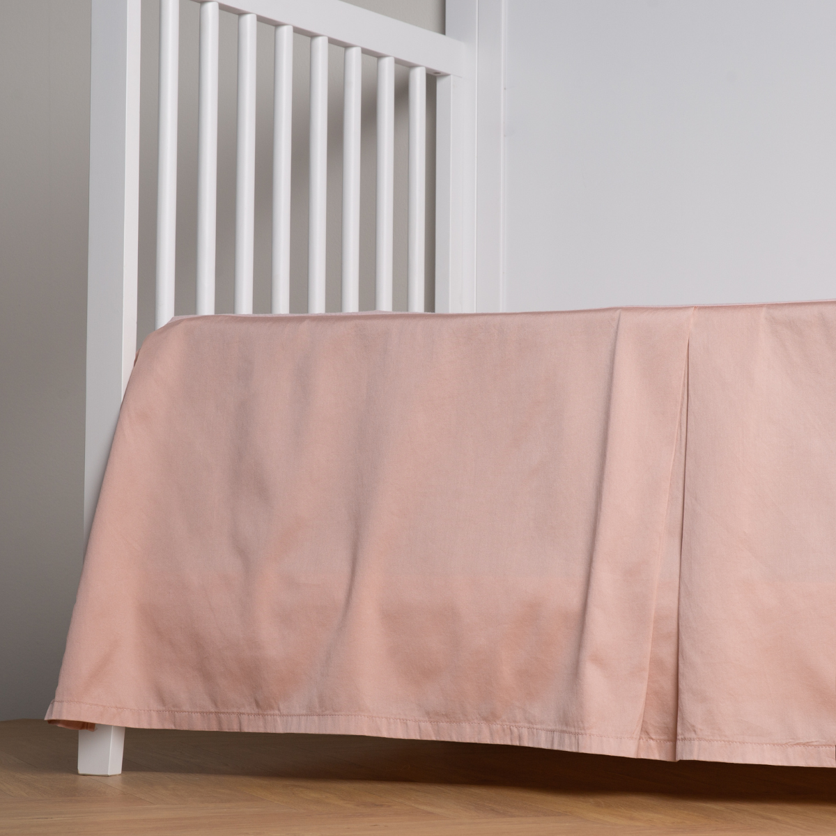 Rouge: cotton sateen cribi skirt with a center pleat shown straight on from a slight angle in a crib without a crib mattress. 