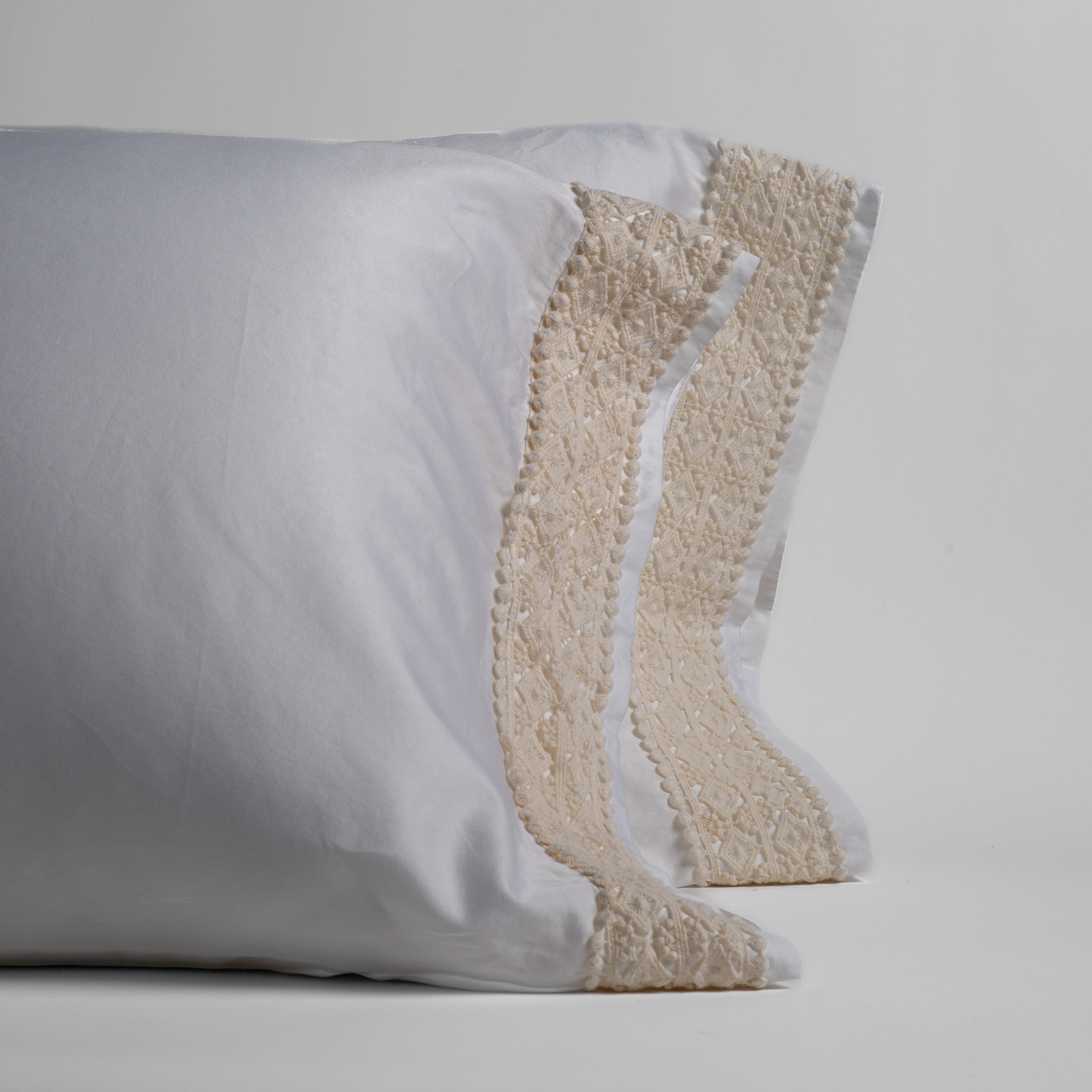 A pair of lace trimmed cotton sateen pillowcases shown standing upright against a white background. 