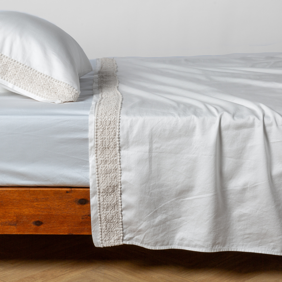 Matching lace trimmed cotton sateen flat sheet and pillowcase shown with a winter white fitted sheet - side view. 