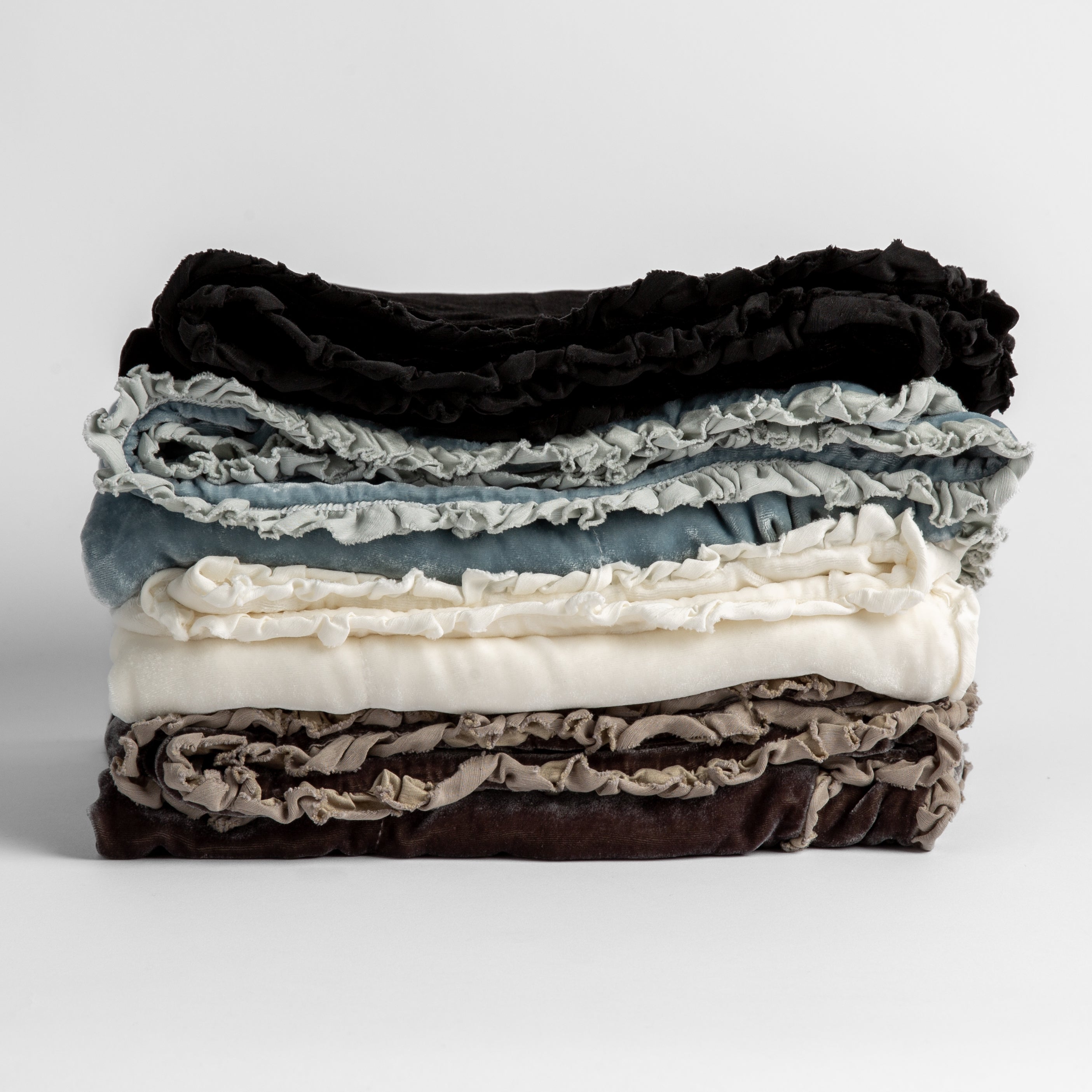 : Stack of four silk velvet baby blankets with charmeuse trim shown against a white background.  Blankets shown in Corvino, Cloud, Winter White and Moonlight. 