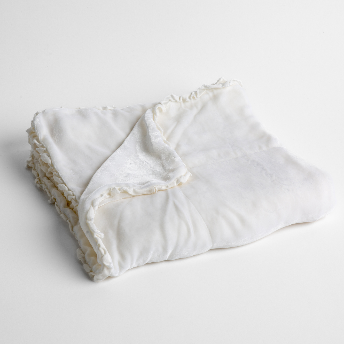 White: silk velvet baby blanket with charmeuse trim shown slightly overhead with a corner folded back to show trim detail against a white background. 