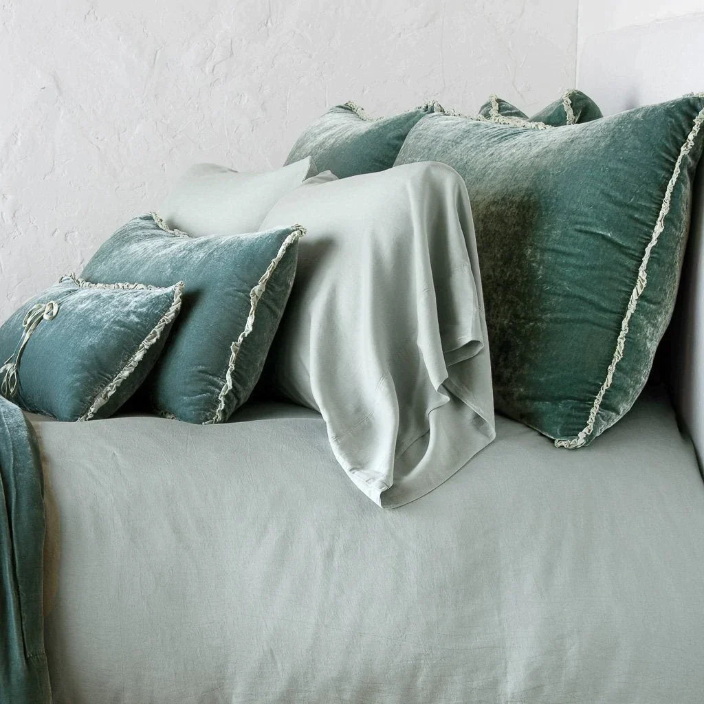 Eucalyptus: Silk velvet shams with a petite ruffle on monochromatic bed, leaning upright behind sleeping and throw pillows - side view.