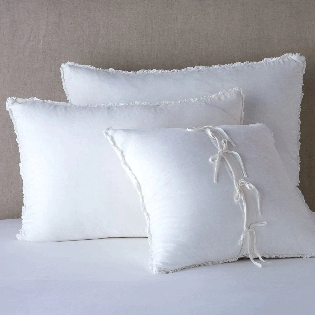 White: : Silk velvet  shams with a petite ruffle leaning upright against a neutral headboard. The front sham is backwards, showcasing the charmeuse tie closures.