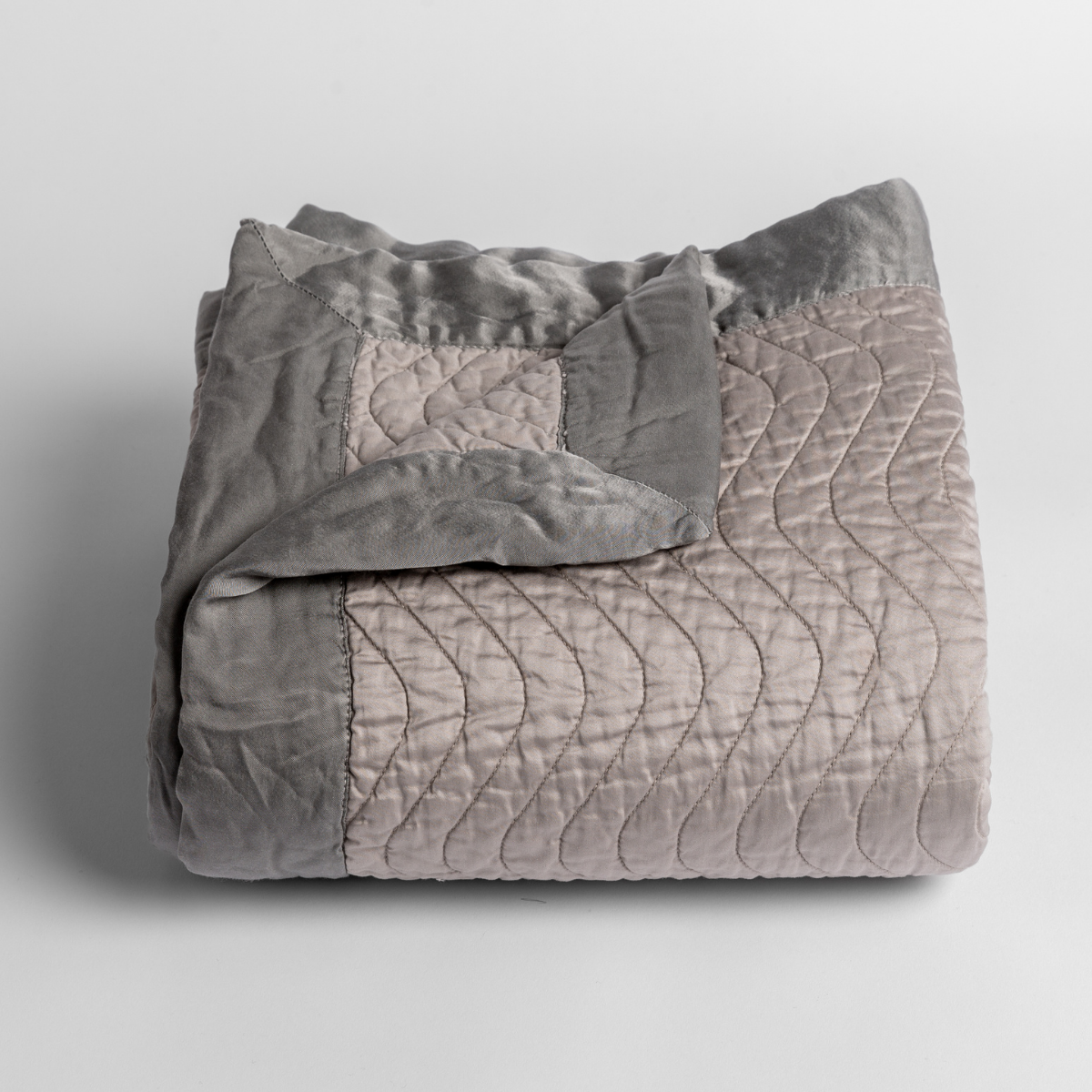Fog: a folded quilted cotton sateen baby blanket with its corner folded down to show the trim contrast - shot against a white background. 